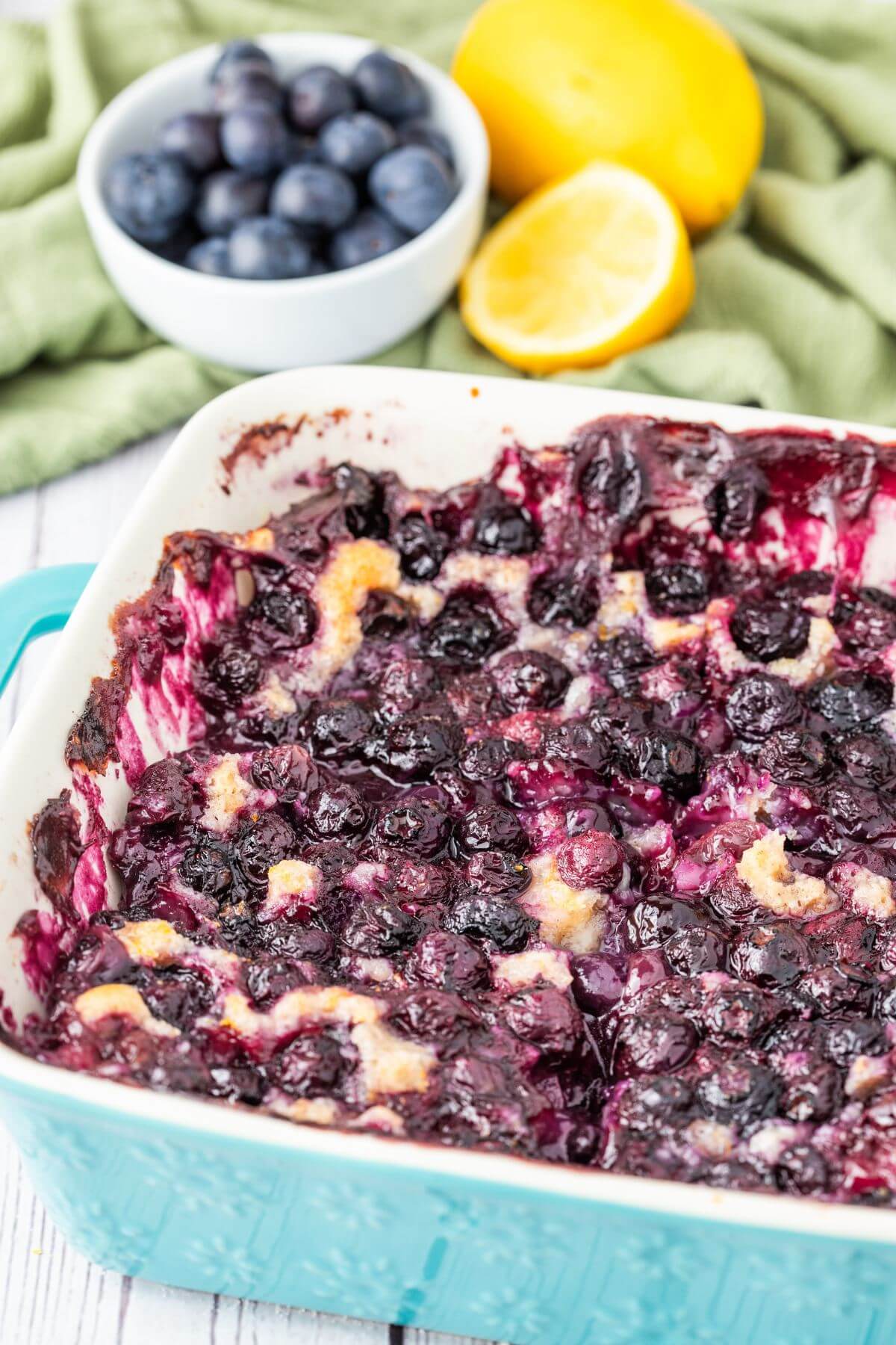 A full pan of baked cobbler with berries sits next to more fruit on table.