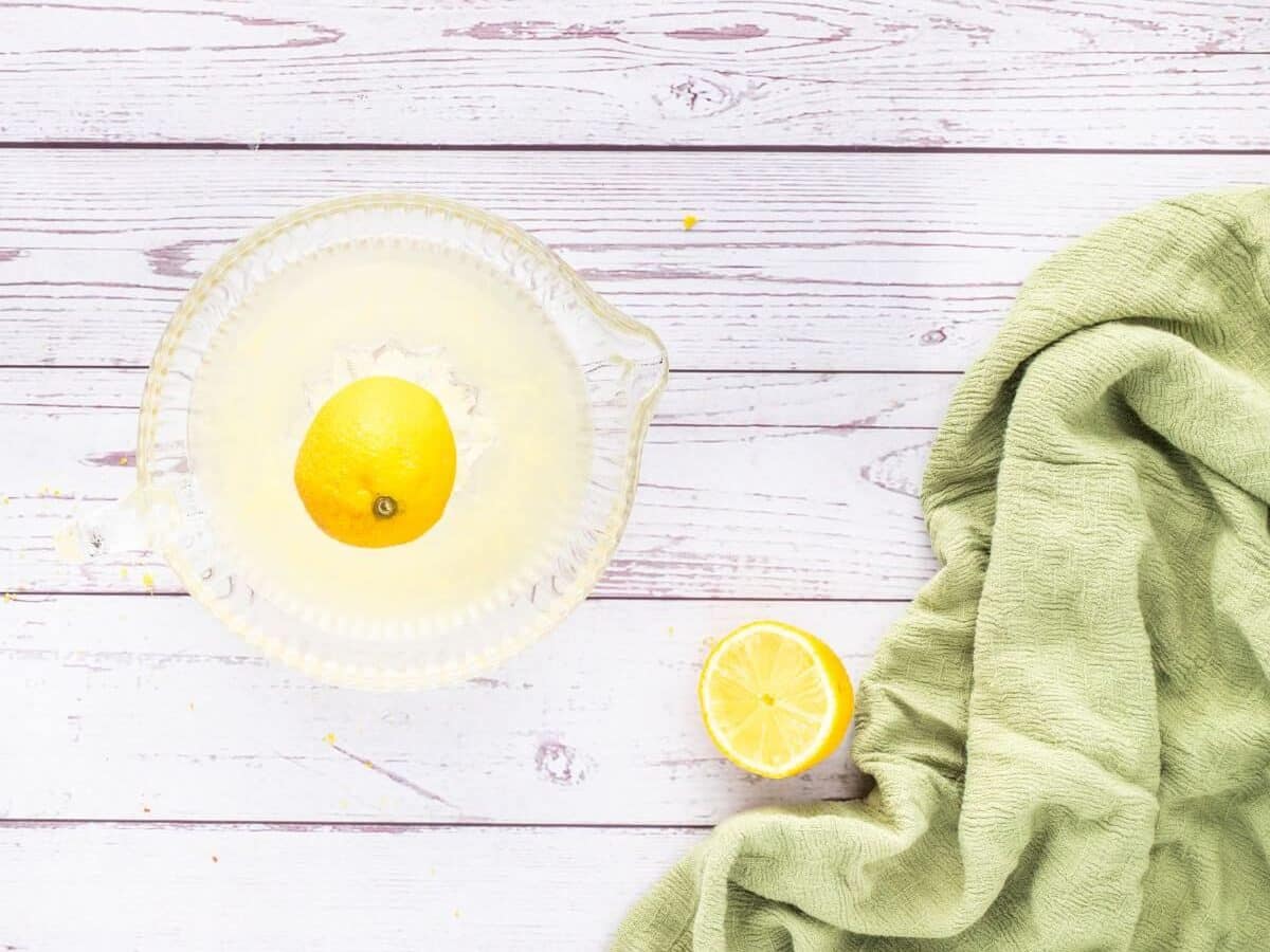 Half of a lemon sits on a table with the other half on top of a juice collector.