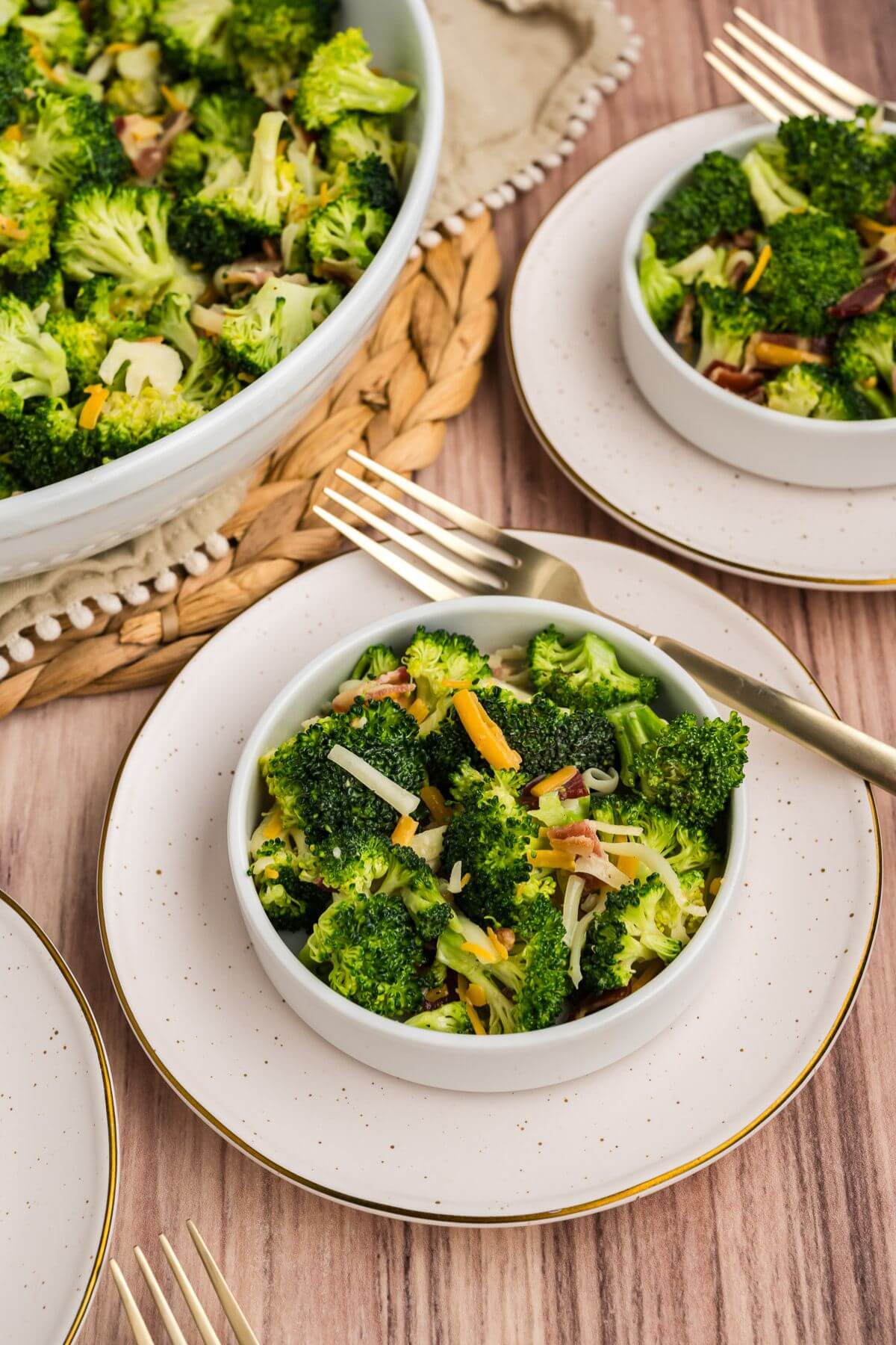 Bright green broccoli is mixed with bacon and cheese and served in small bowls on saucers.