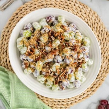 A white plate on wicker place mat is filled with grapes, pecans, and seasoning.
