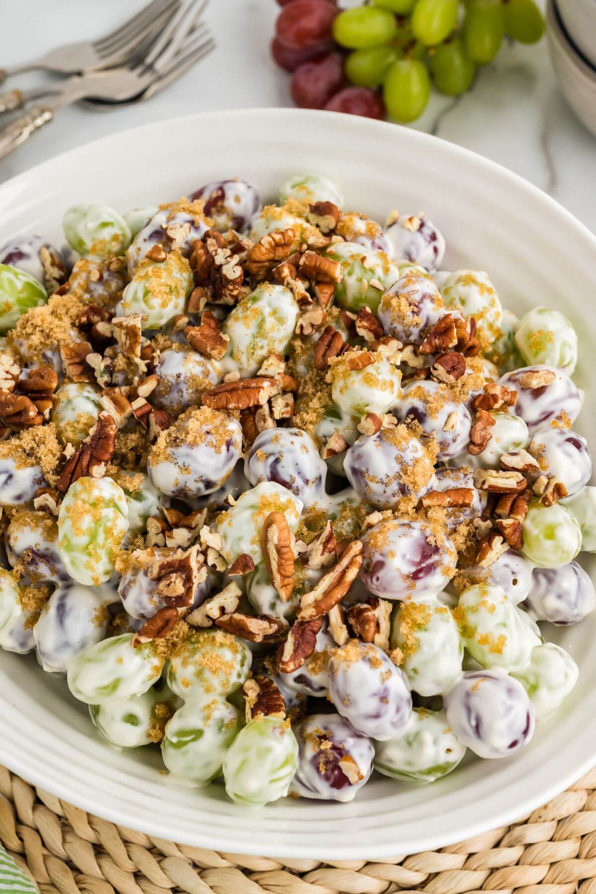 Silverware and extra grapes sit next to a full white plate of seasoned grapes with cream cheese and pecans.