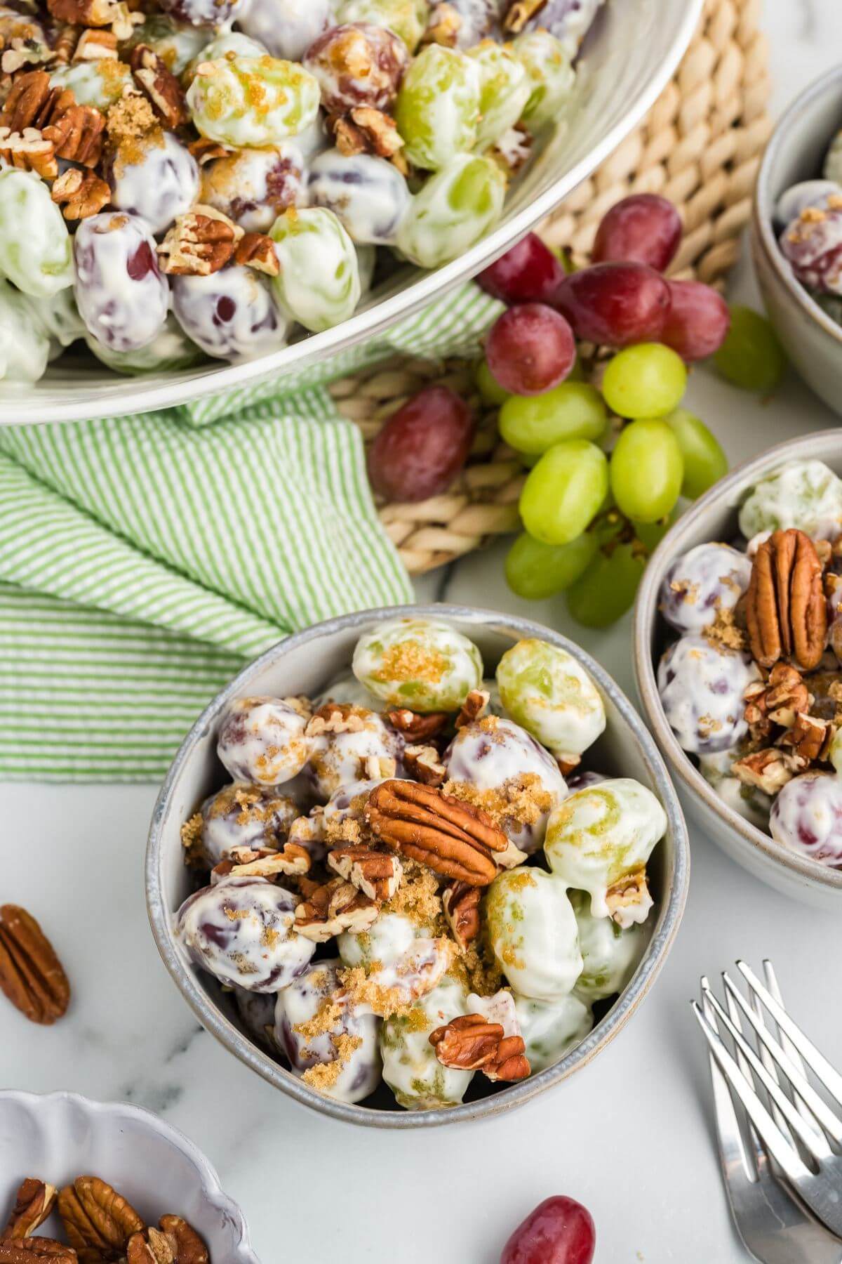 Smaller serving bowls of grape salad sit next to a giant bowl of the same.