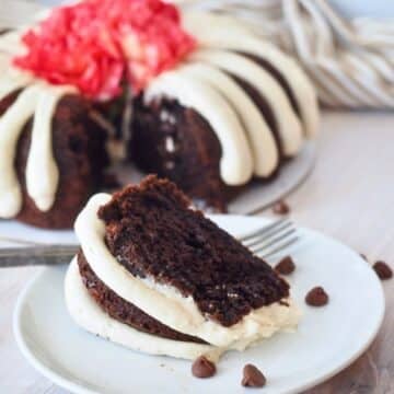 Slice of chocolate chip bundt cake with fingers of frosting and whole cake in background.