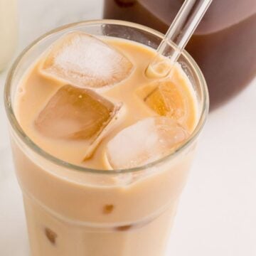 Light brown chai and milk is blended together for a smooth drink in a glass with straw.