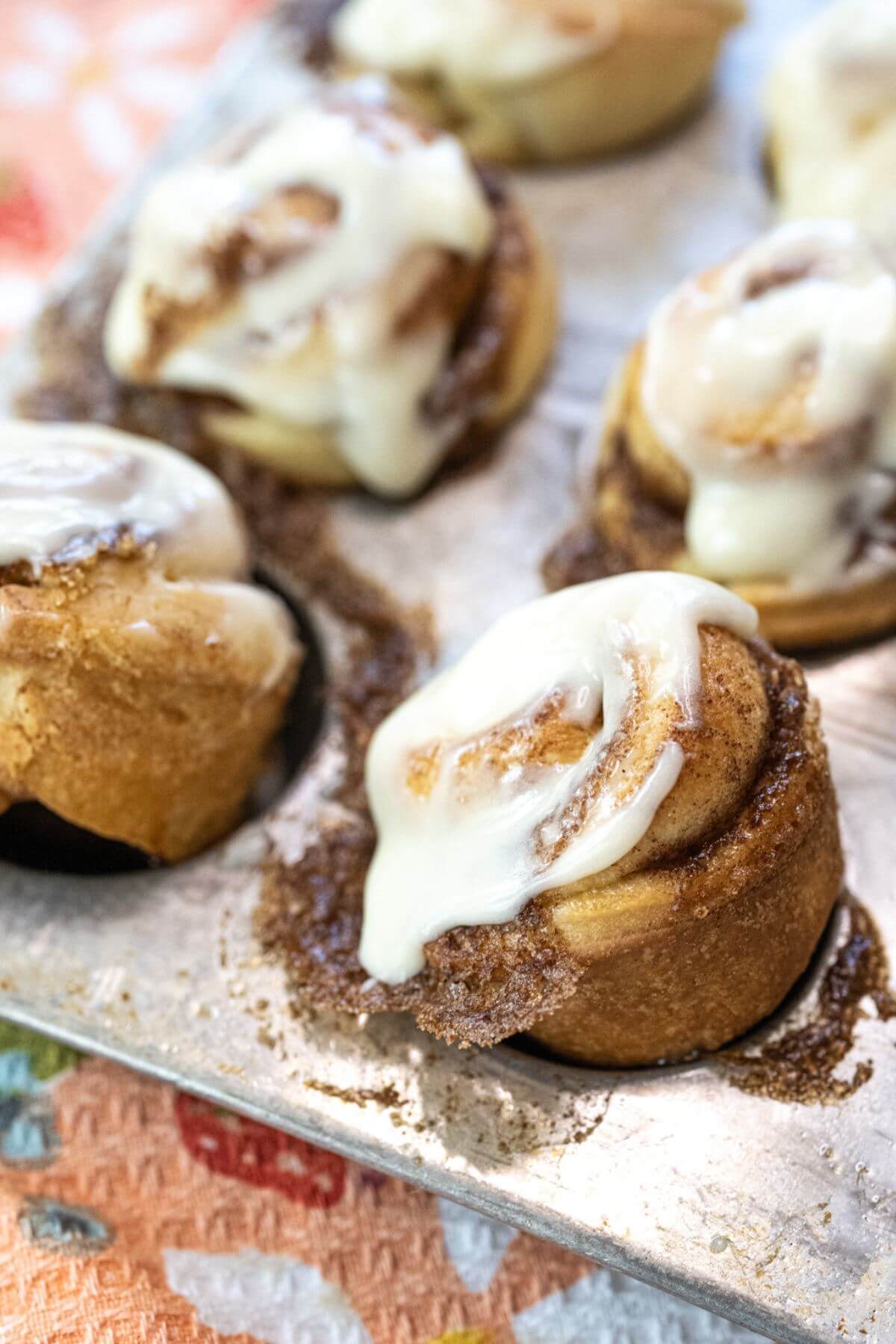 Small cinnamon buns sit angled on a metal sheet.