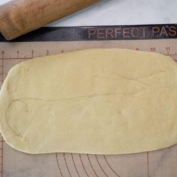 Flattened dough sits on a rolling board by a rolling pin.