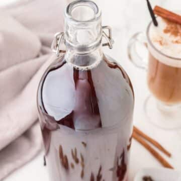 Chai concentrate in large flip-top bottle with a homemade chai latte behind it.