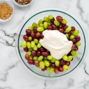 A glass bowl is filled with mixed red and green grapes with a blob of white dressing on top.