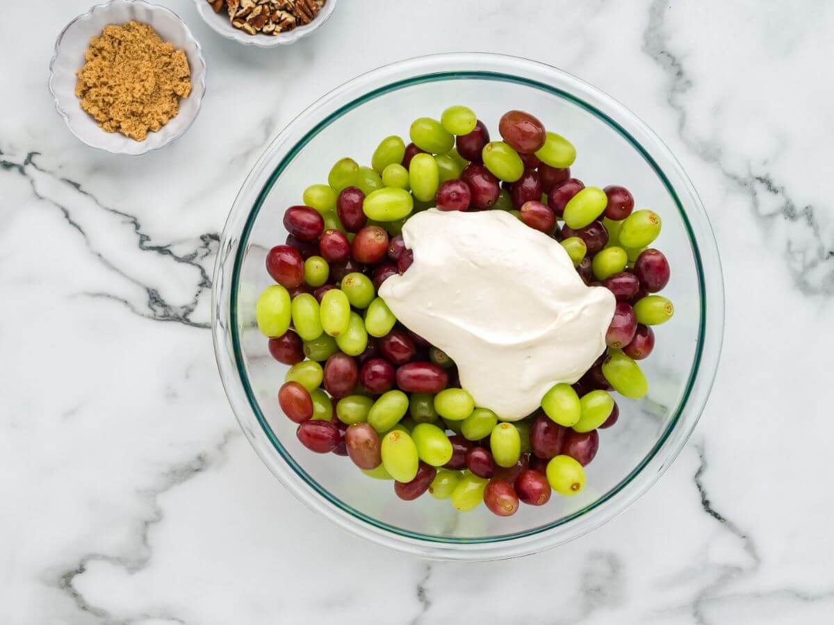 A glass bowl is filled with mixed red and green grapes with a blob of white dressing on top.