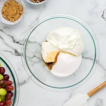 A glass mixing bowl holds cream cheese, sour cream, and sugars.