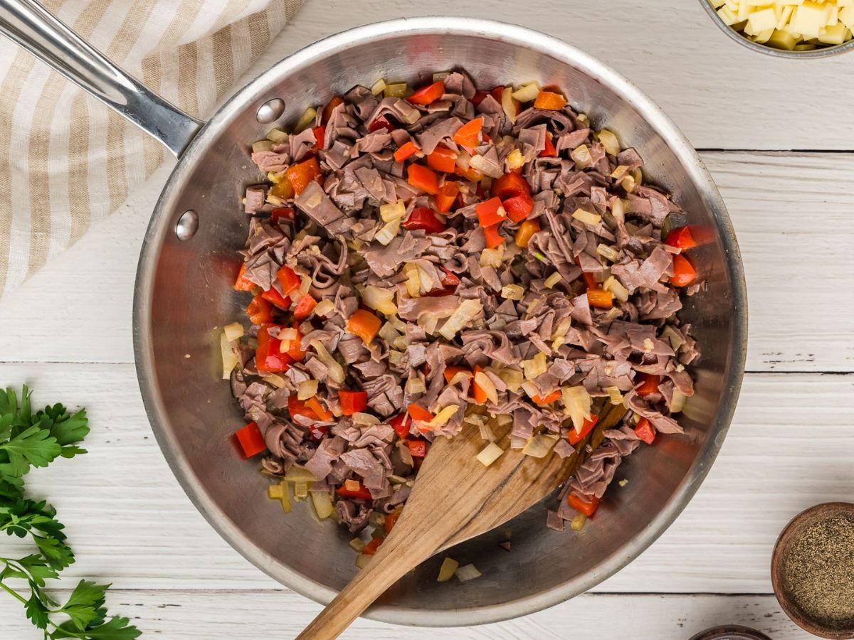 Roast beef, onions, peppers and seasonings sauteeing in a pan. 