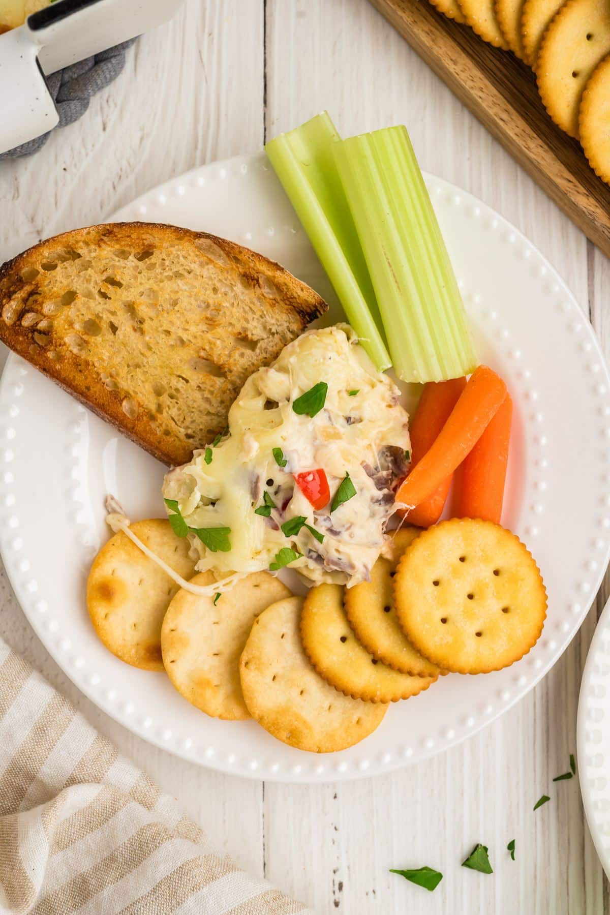 Steak and cheese dip on a plate with toasted bread, crudite and butter crackers.