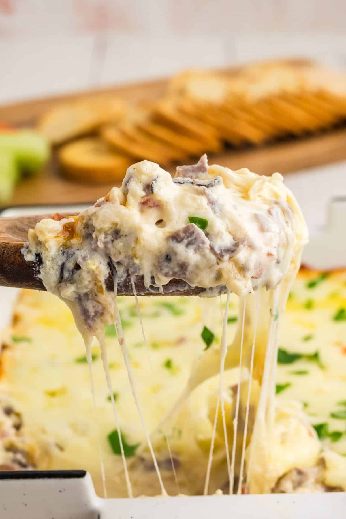 Wooden spoon with scoop of Philly cheesesteak dip with stringy cheesepull.