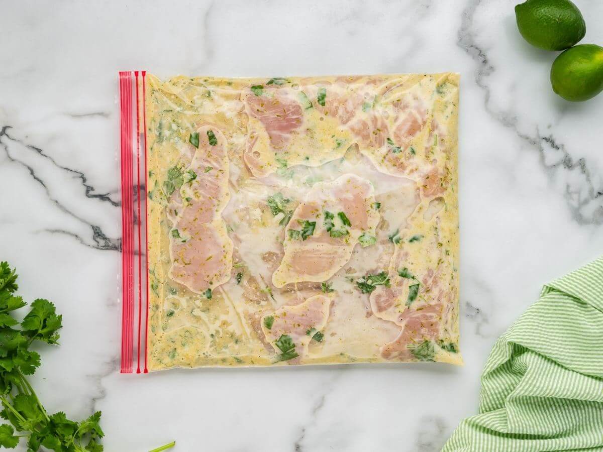 Uncooked chicken breasts sit in a freezer bag filled with a yellow creamy marinade.
