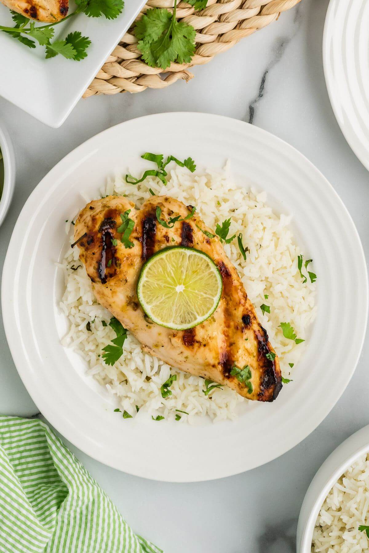 White plates and wicker placemats hold grilled chicken and rice.