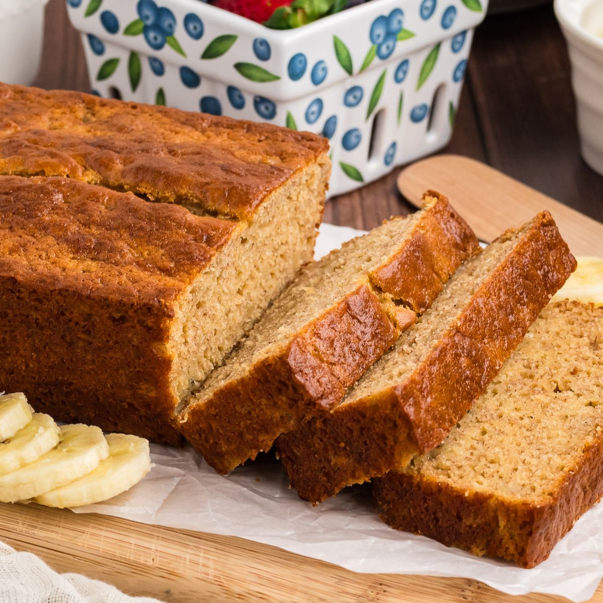 Sourdough discard banana bread sliced on a breadboard with sliced bananas nearby.