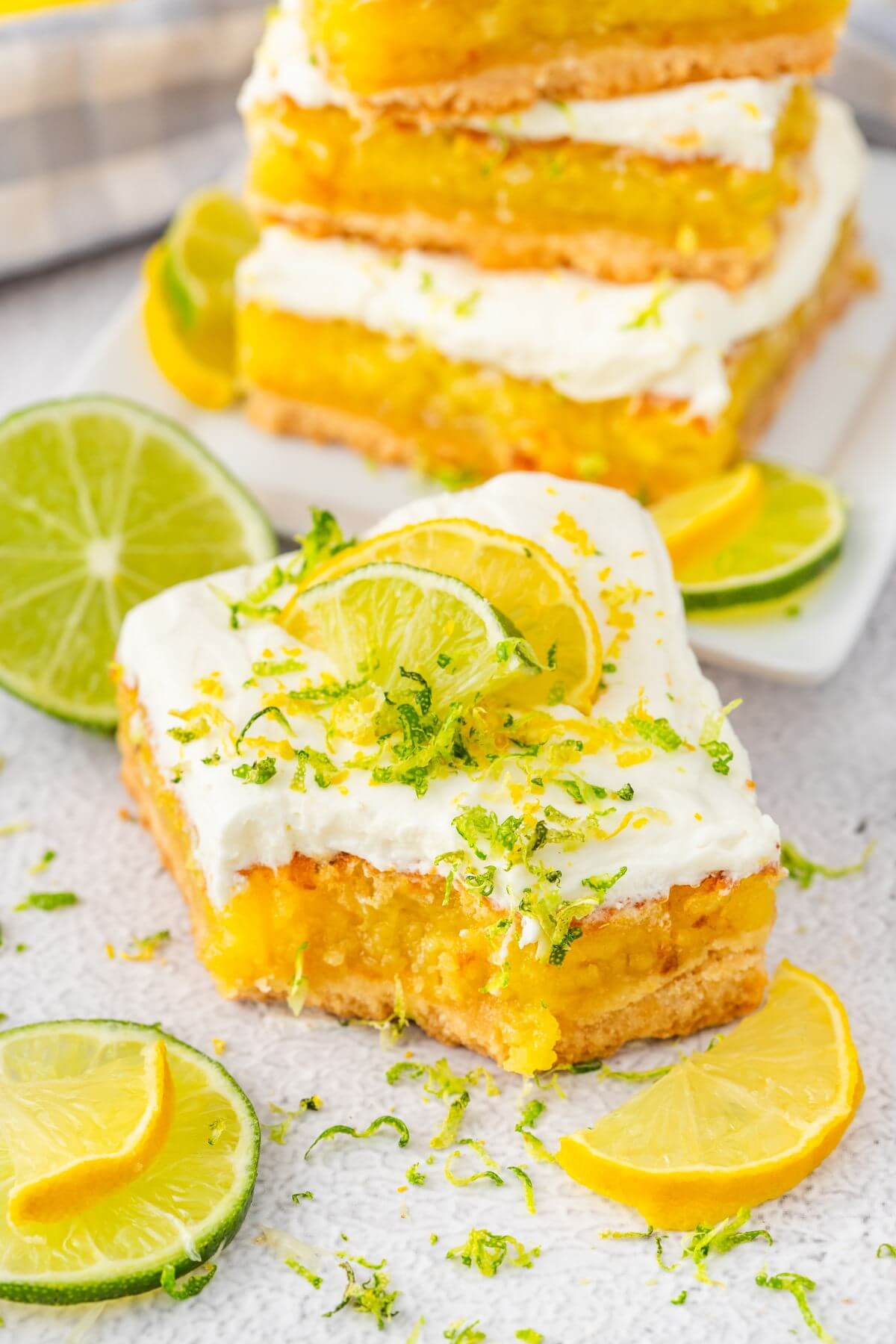 A dessert bar has a bite removed from its corner and rests in front of a stack of more bars and lemon and lime slices.