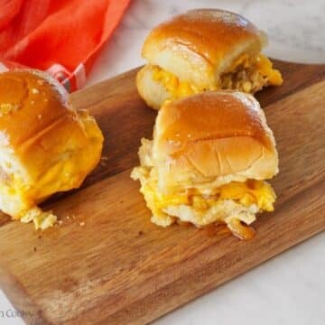 3 breakfast sliders on a cutting board with melty cheese.
