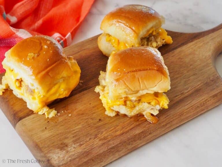 3 breakfast sliders on a cutting board with melty cheese.