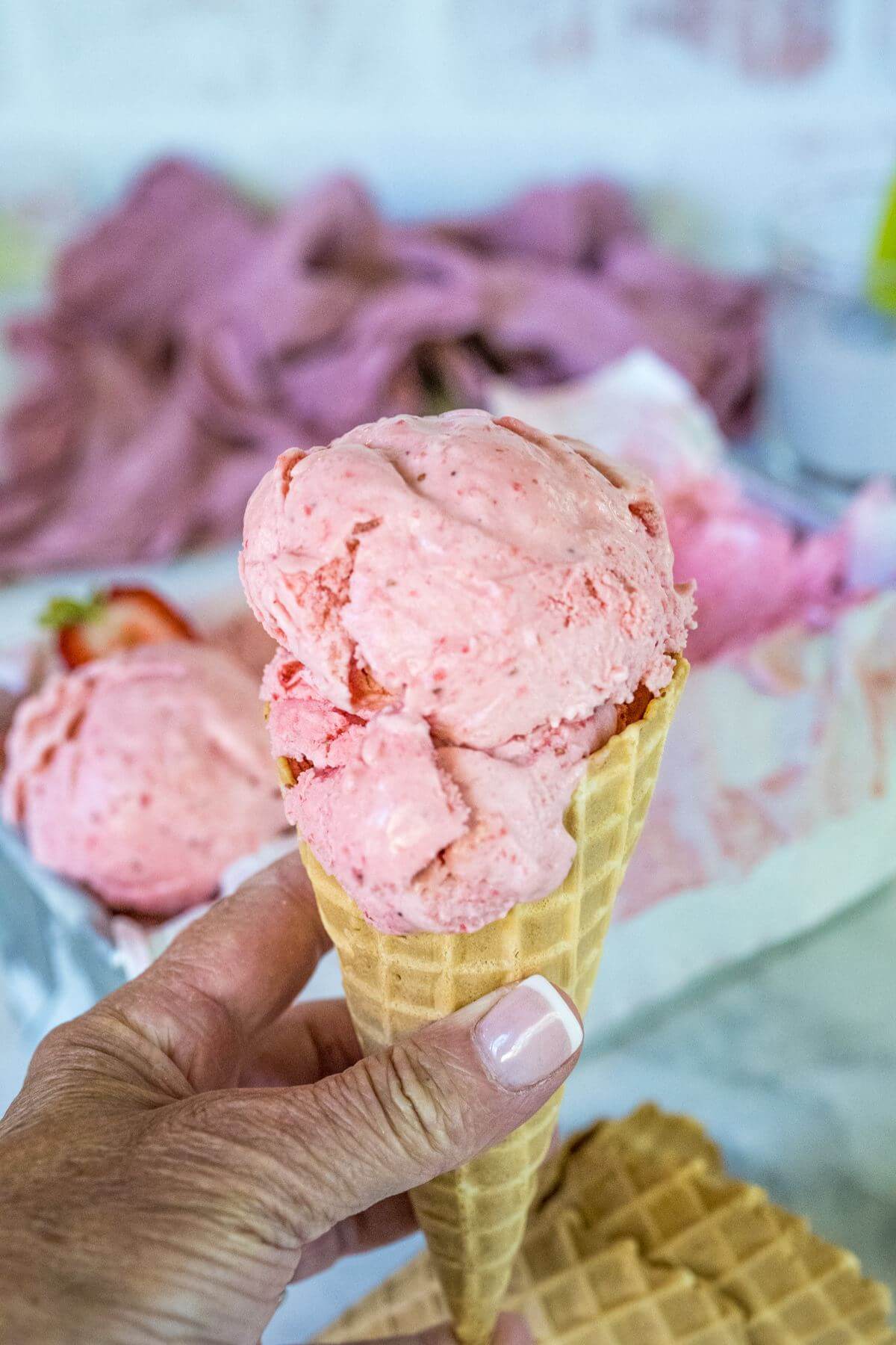 Hand holding a scoop of homemade strawberry ice cream on a waffle cone. 