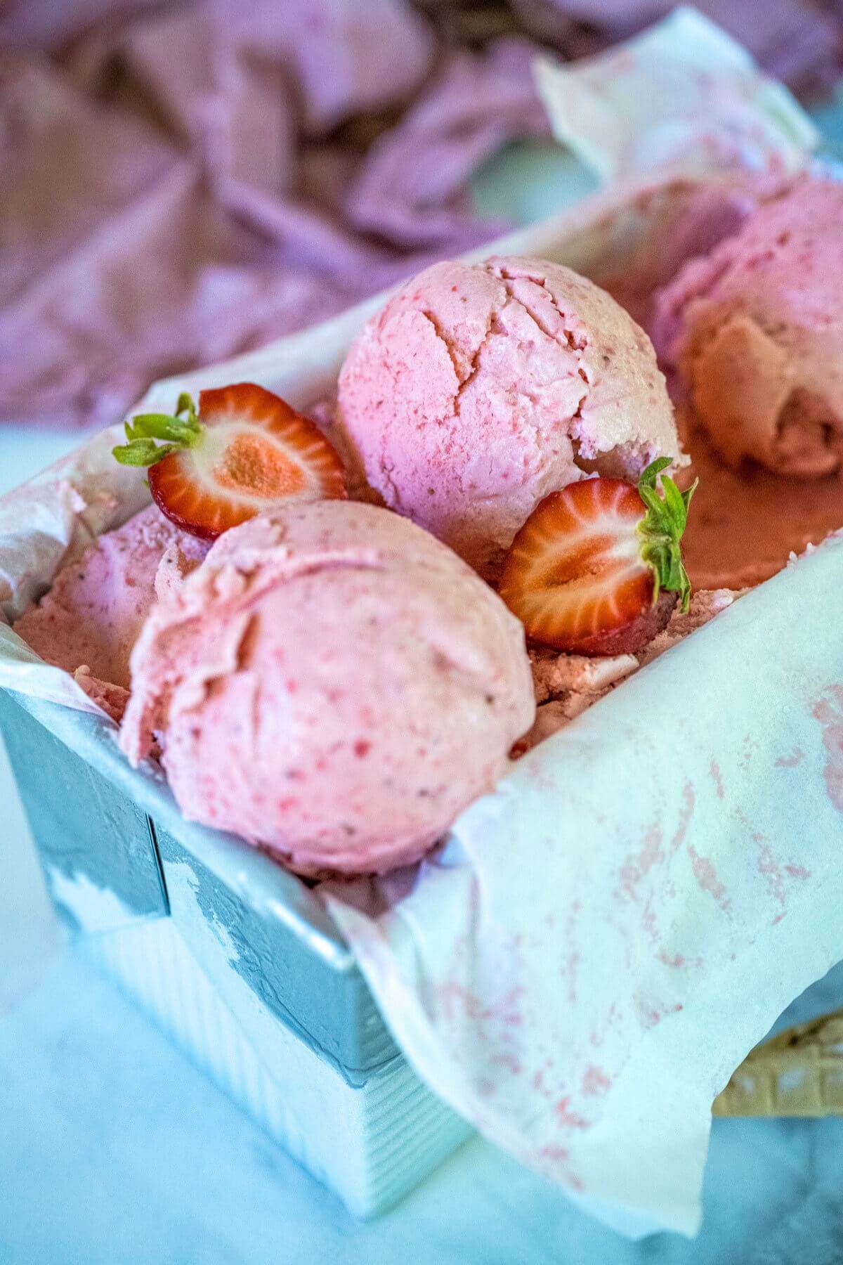 Strawberry Ice cream with scoops on top of the container of ice cream. 