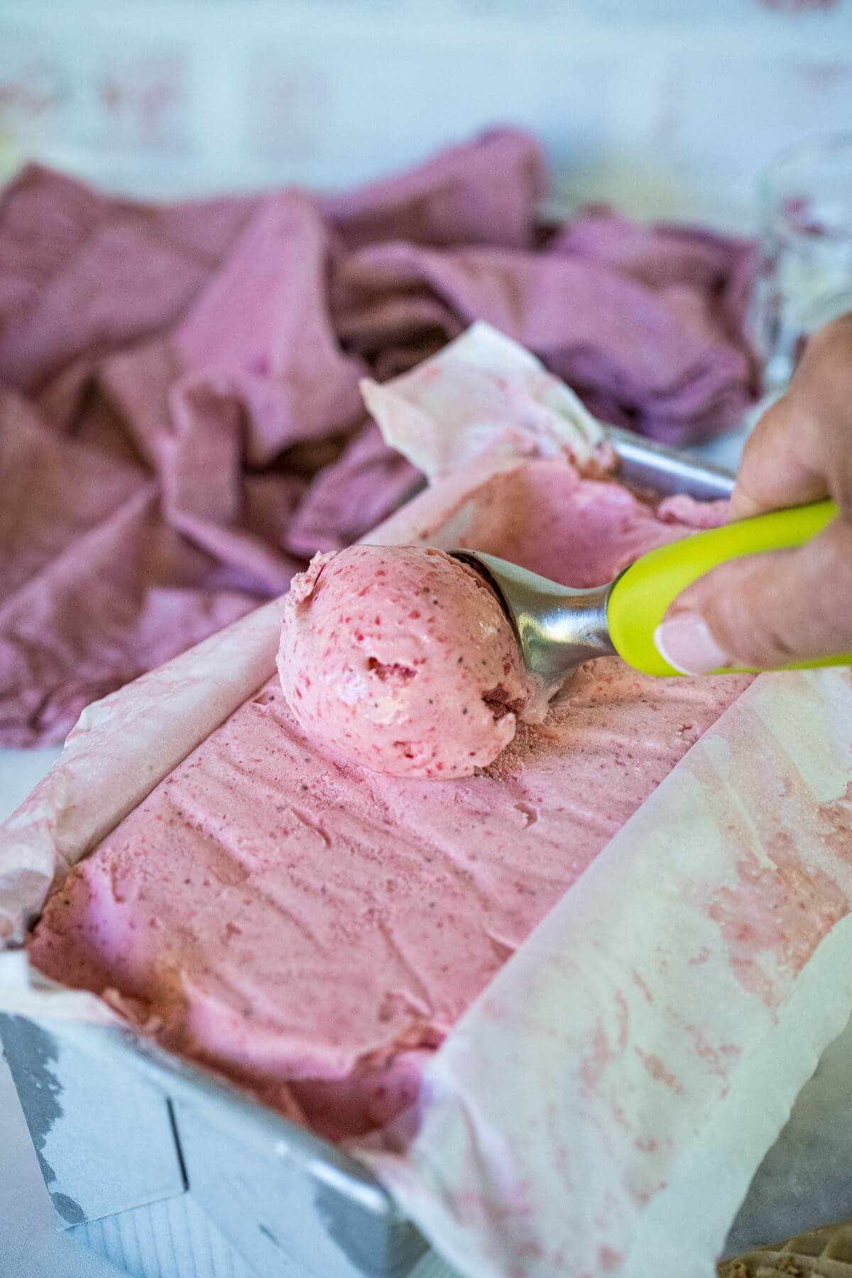Strawberry gelato in container, hand pulling a scoop of ice cream.