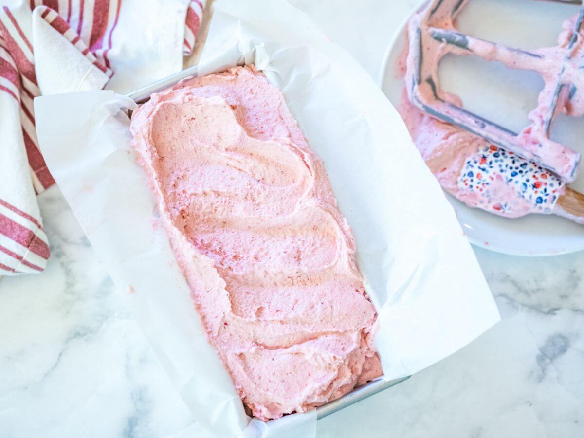 Creamy strawberry ice cream scooped into a parchment lined loaf pan.