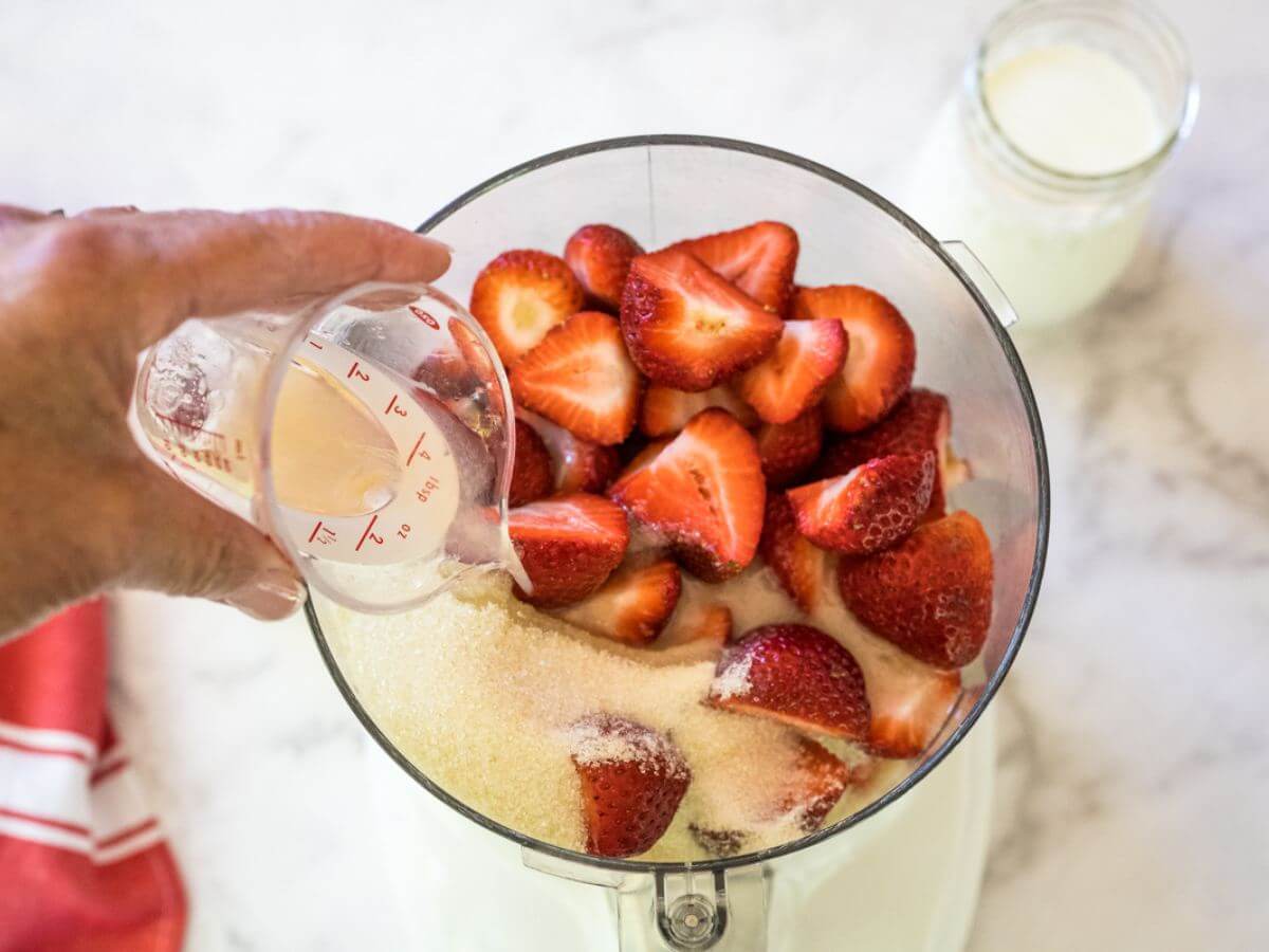 Adding vanilla and lemon juice to the strawberry sugar mixture in food processor.