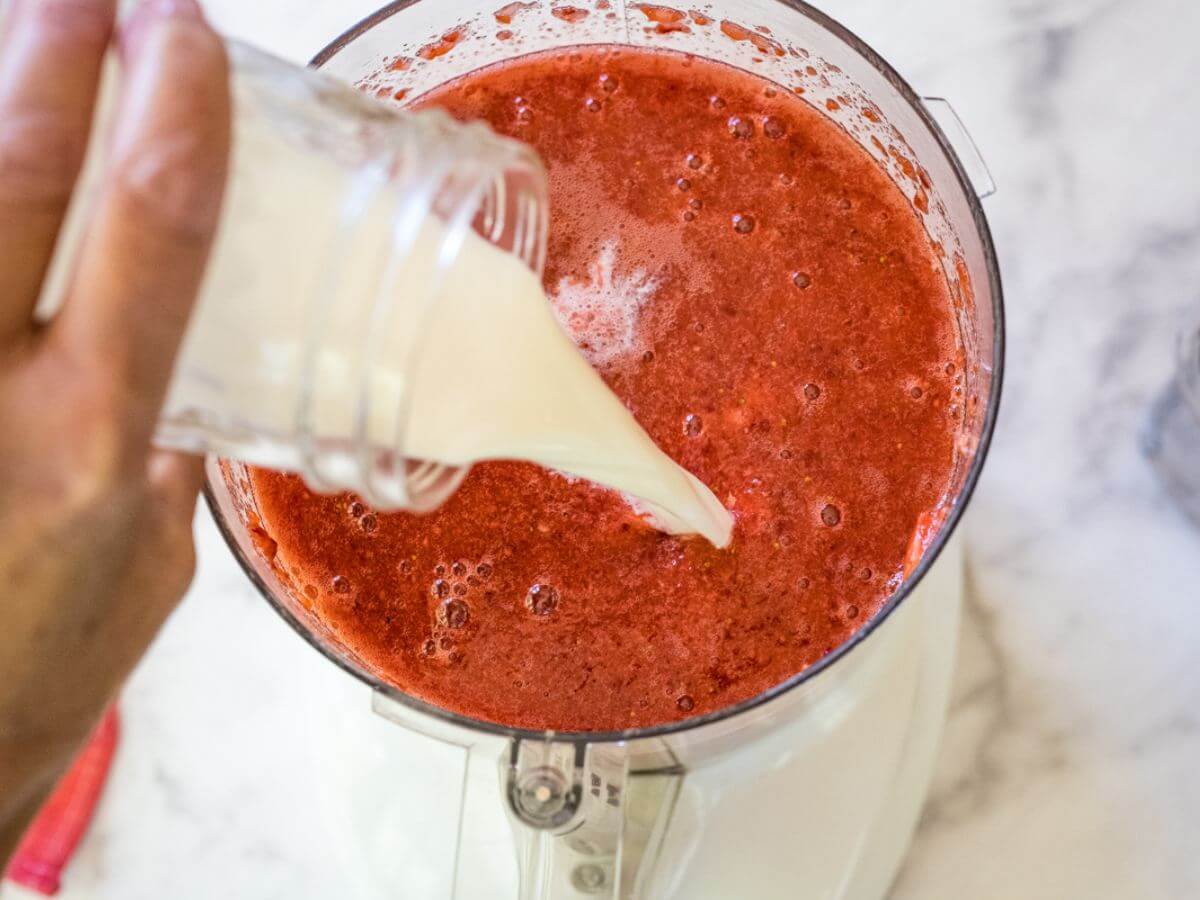 Pouring milk into strawberry mixture in food processor.