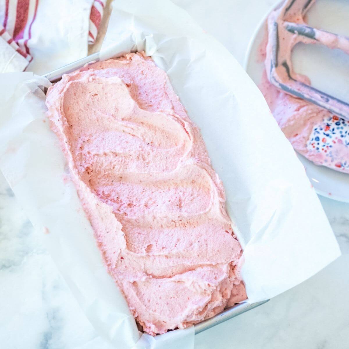 Creamy strawberry ice cream in a loaf pan container lined with parchment paper.