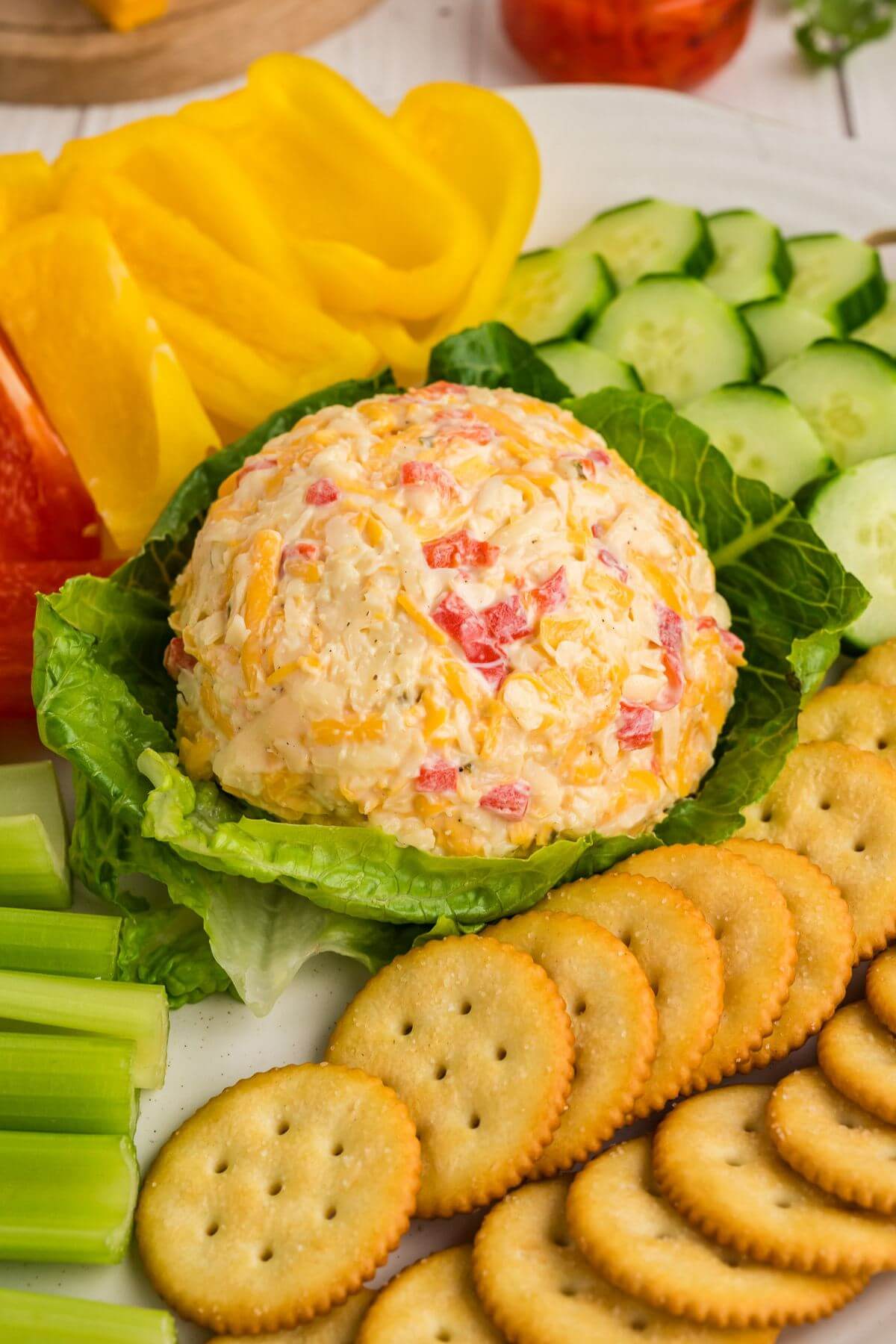 Pimento cheese ball served on a lettuce leaf with prepped vegetables and crackers surrounding it.