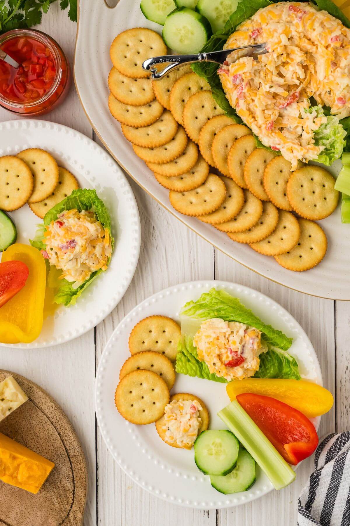Pimento cheese spread served on a large platter with crackers and veggies with two plates next to it.