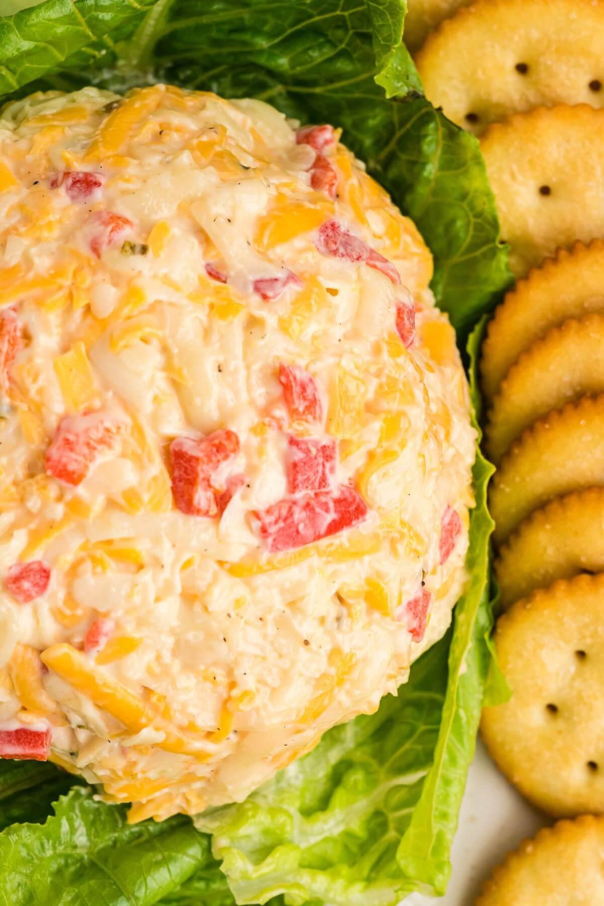 Pimento cheese ball served on a lettuce leaf with crackers on the side.