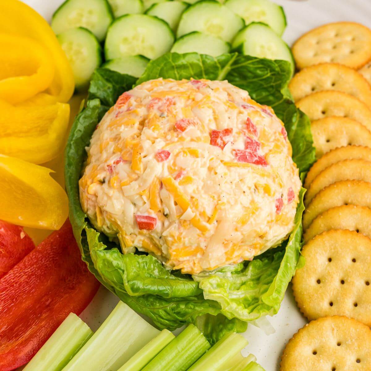 Pimenot cheese shaped into a small ball on a plate with crackers, and veggies. 