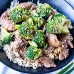 Beef and Broccoli in a black bowl with rice and sauce on top.