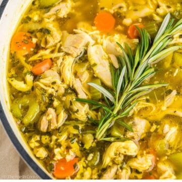 Homemade chicken soup in a stock pot with a fresh rosemary sprig on top.