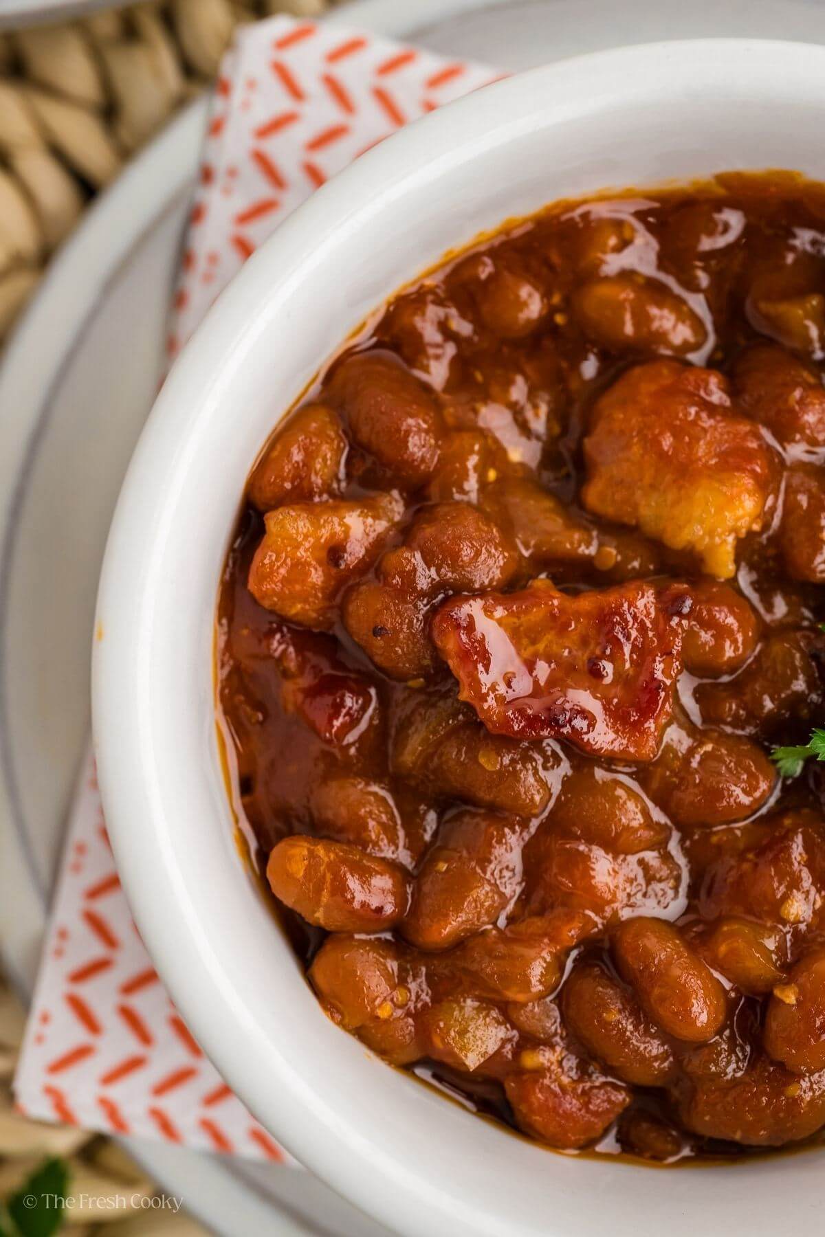 Cowboy baked beans close up highlighting crispy bacon topping. 