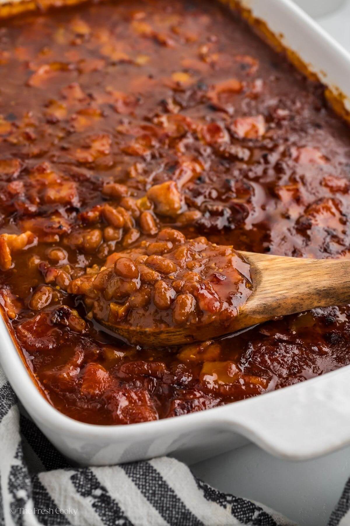 Cowboy baked beans in a casserole baking dish with a spoon serving. 
