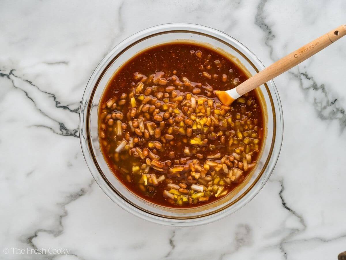 All ingredients for cowboy bacon baked beans in a large bowl, being stirred.