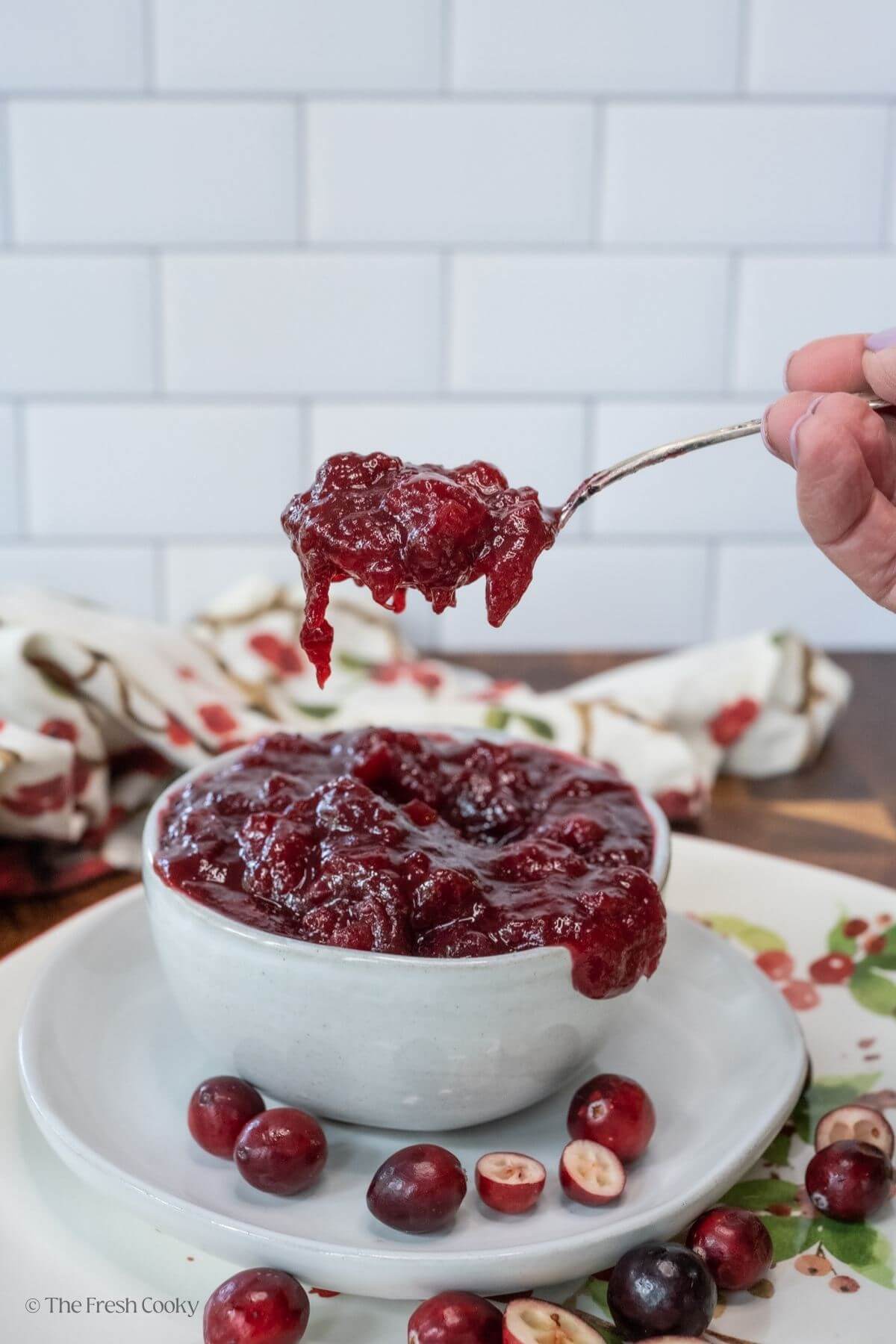 Hand holding a spoon of cranberry sauce over a bowl full of cranberry sauce.