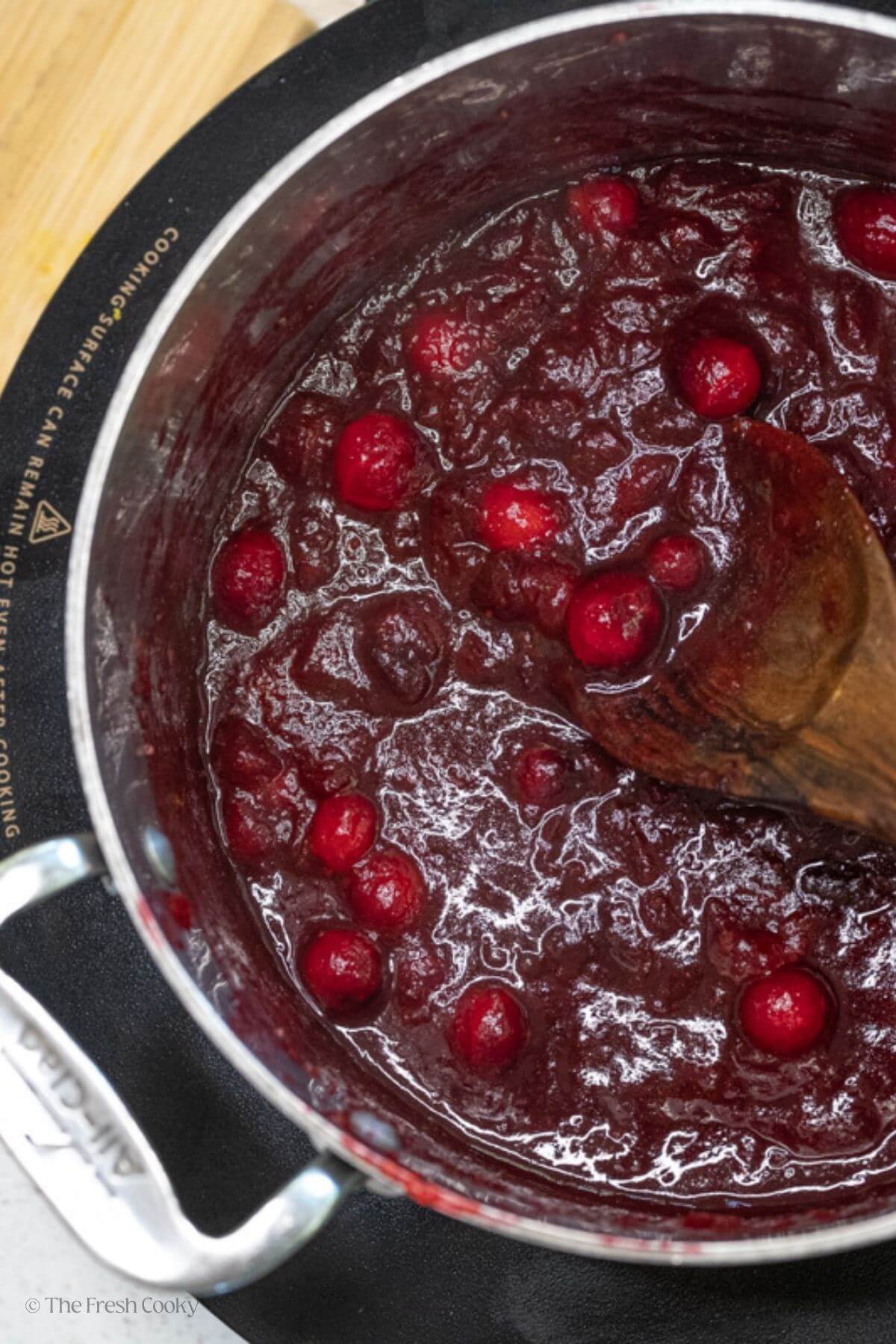 Cranberry sauce cooking in a large silver pot with a wooden spoon.
