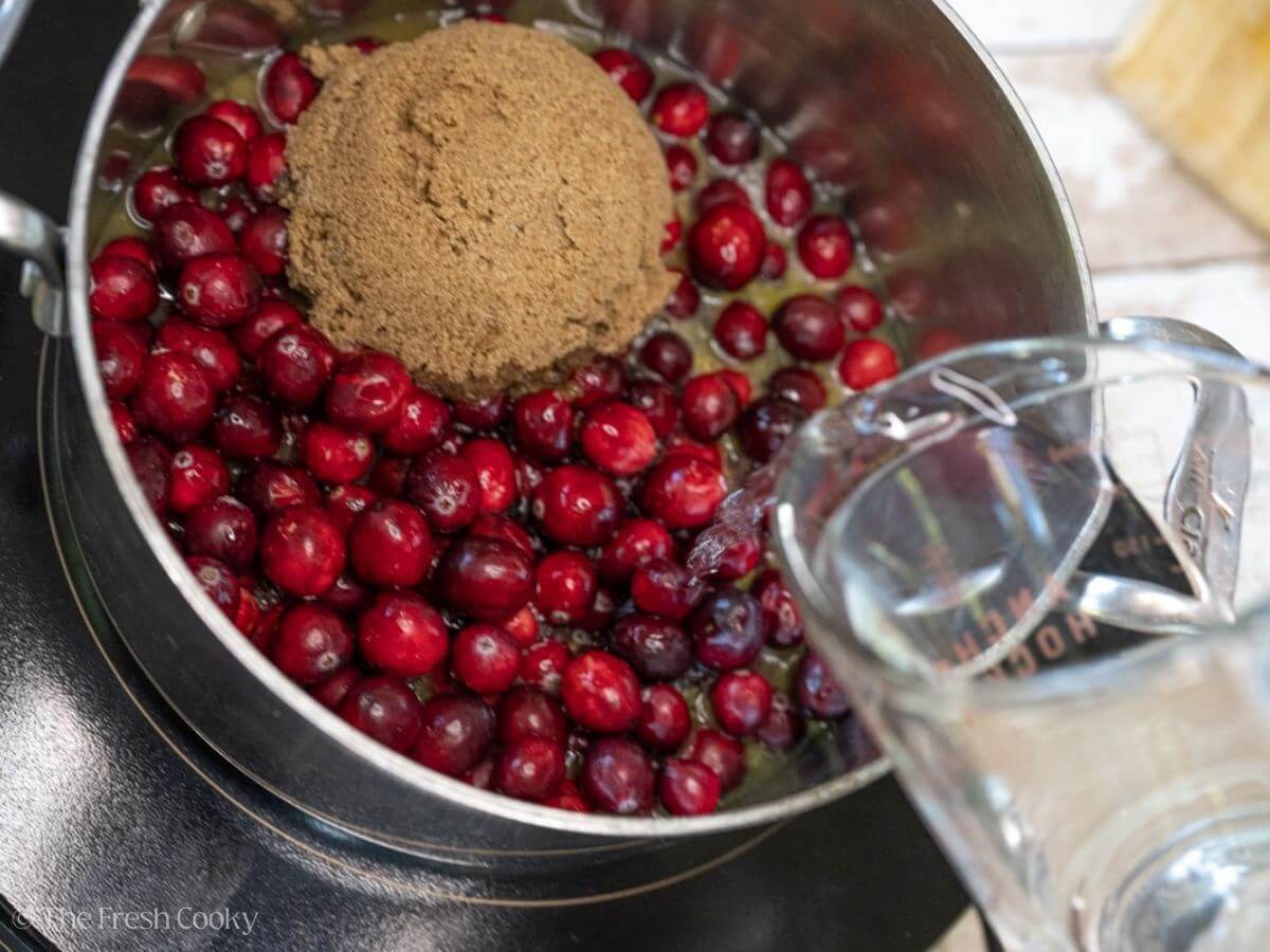 Adding water to the cranberry mixture in a pot.
