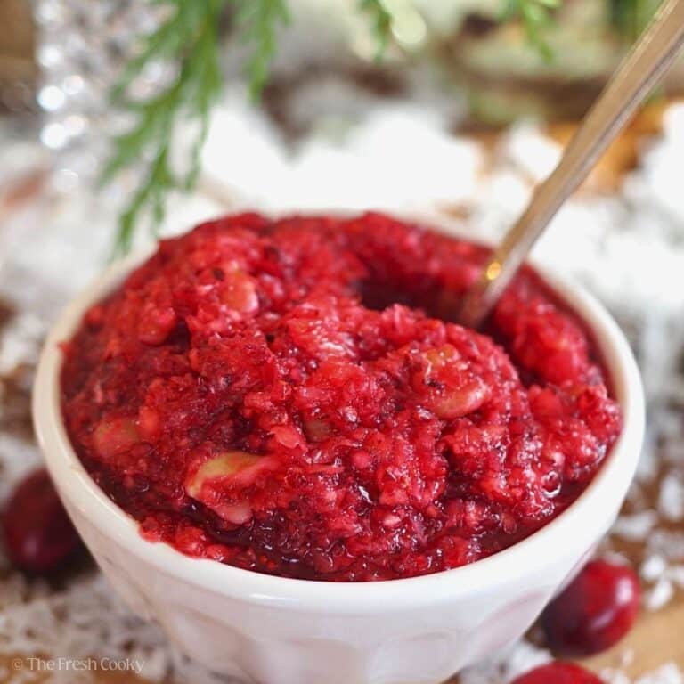 A small bowl of fresh cranberry relish on a fresh cranberry strewn surface.