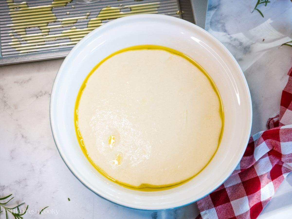 Focaccia dough in a mixing bowl with olive oil after rising.