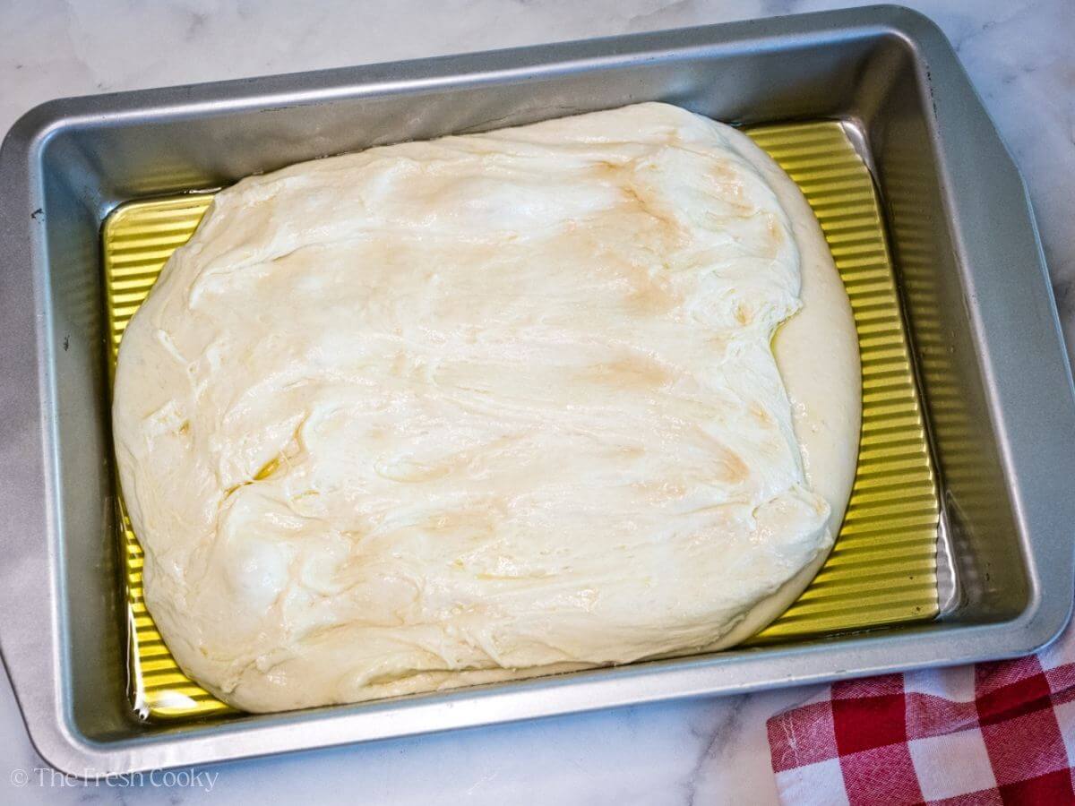 Focaccia dough in a baking dish with olive oil.