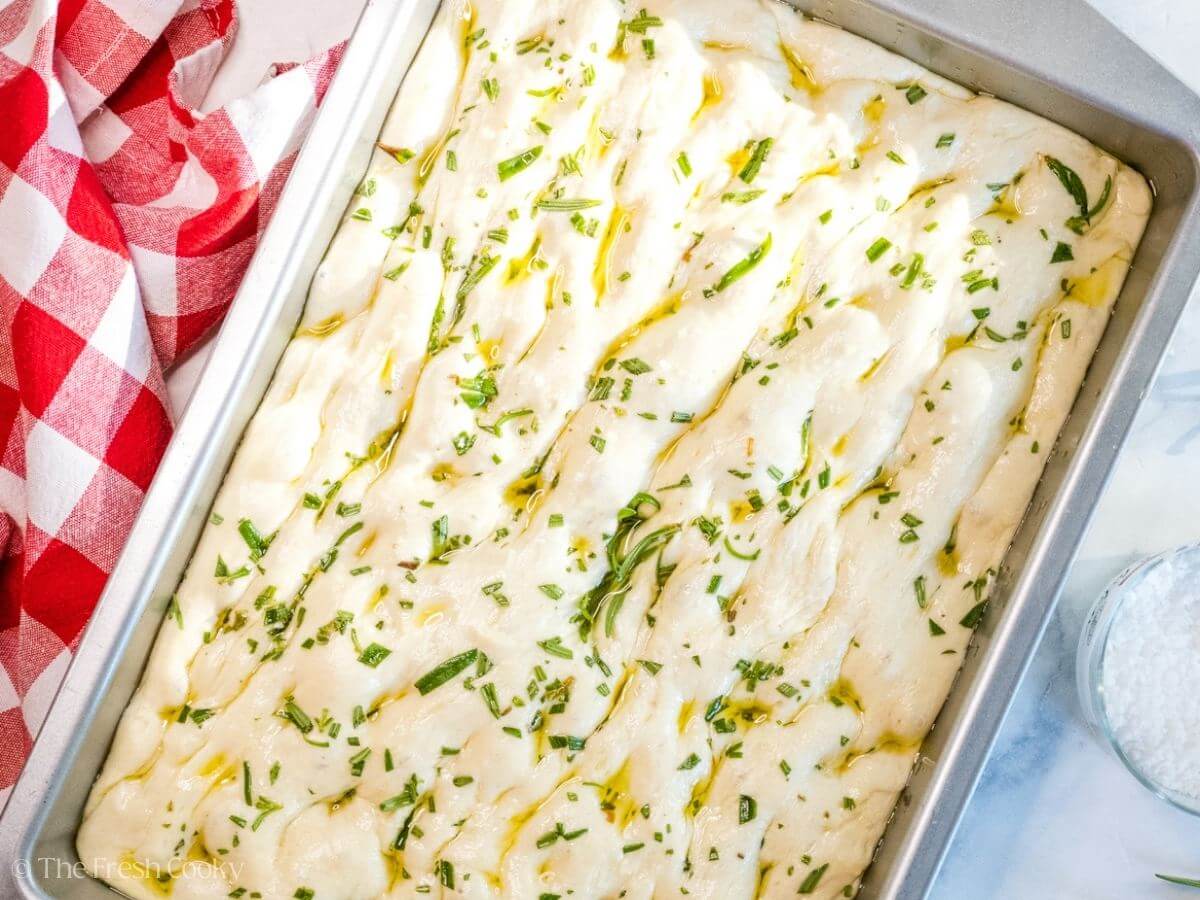 Focaccia dough in a baking dish topped with olive oil, salt and rosemary after rising.