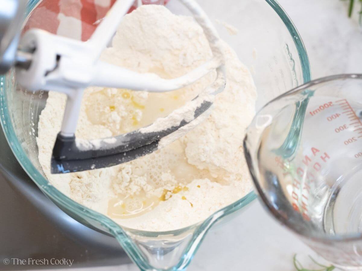 Pouring water in to the dry ingredients in a stand mixer bowl.