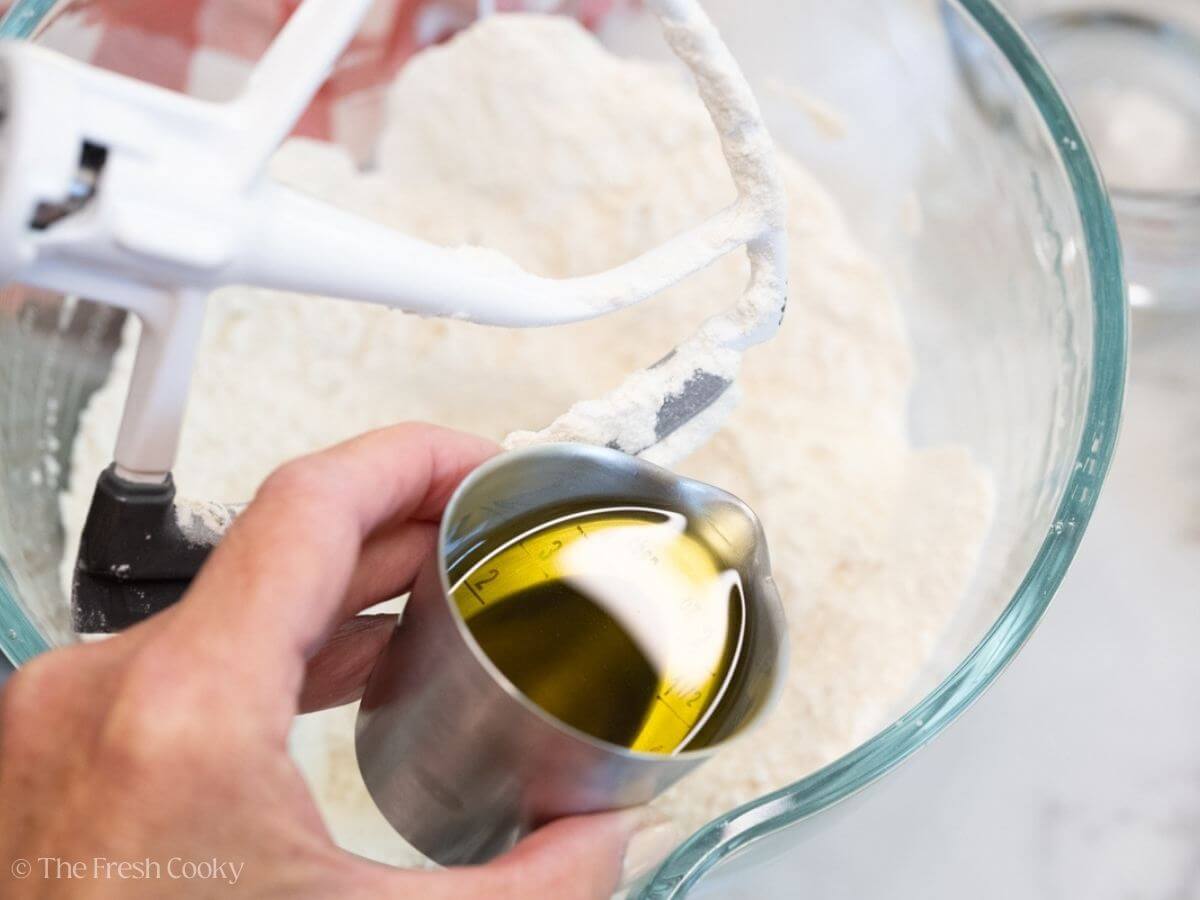 Pouring olive oil in the the dry ingredients in a stand mixer bowl.