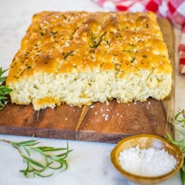 Fluffy focaccia bread on a wooden cutting board with some sliced off the end.