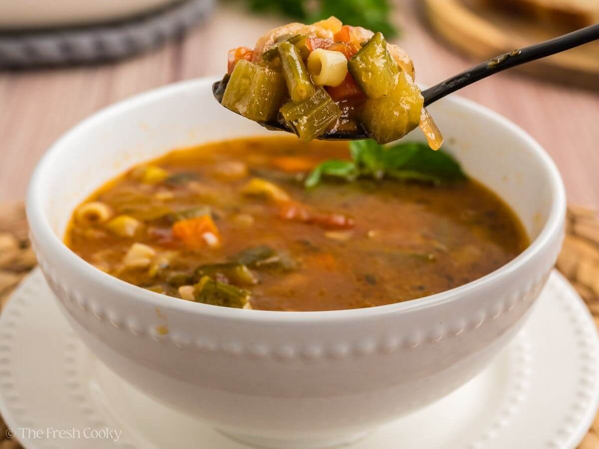 Spoonful of minestrone soup coming from a bowl of soup.